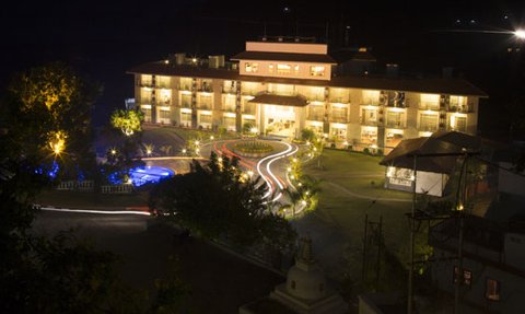 Ein elegantes Resort am Wasser, beleuchtet von warmem Licht, umgeben von üppigem Grün und einem klaren Nachthimmel.