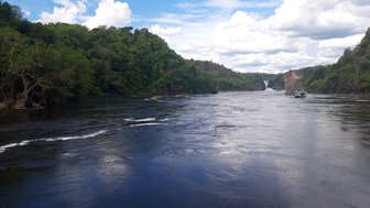 Ein ruhiger Fluss schlängelt sich durch üppige grüne Hügel, während Wolken am blauen Himmel vorbeiziehen.