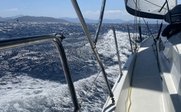 Ein Blick von einem Segelboot auf das glitzernde Wasser und die sanften Wellen unter einem strahlend blauen Himmel.