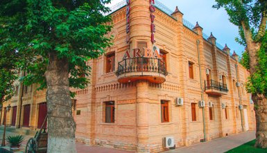 Das Arba Hotel zeigt eine beeindruckende Fassade aus hellen Ziegeln, umgeben von üppigem Grün und einem klaren Himmel.