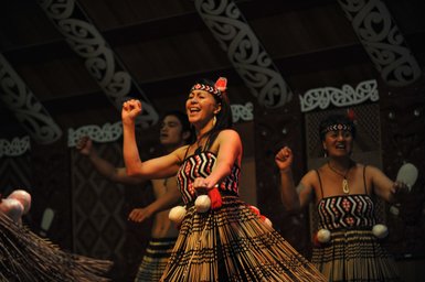 Eine Gruppe von Māori-Tänzern führt einen traditionellen Tanz mit lebhaften Bewegungen und fröhlichen Gesichtern auf.