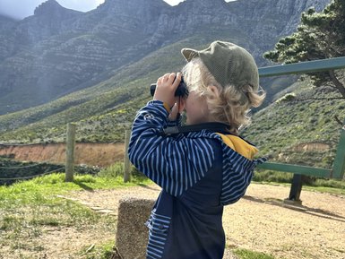 Junge schaut mit Fernglas auf die Landschaft in Hout Bay – Südafrika Familienreise