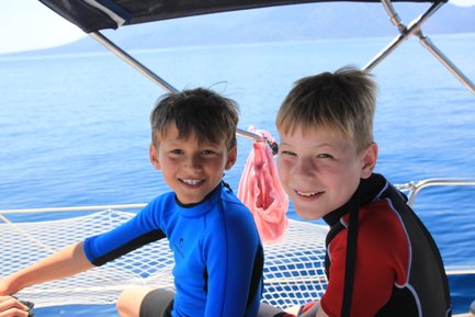 Zwei fröhliche Jungen in Neoprenanzügen sitzen auf einem Boot und genießen die Sonne und das Wasser um sie herum.