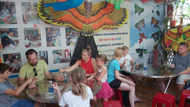 In einem bunten Raum basteln Kinder und Erwachsene gemeinsam Drachen, während sie konzentriert an ihren Projekten arbeiten.