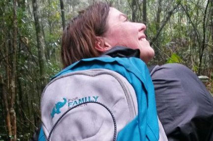 Eine Person mit einem blauen Rucksack lächelt glücklich, während sie durch einen dichten Wald wandert.