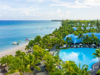 Ein tropisches Resort mit einem großen Pool umgeben von Palmen, Blick auf den klaren Ozean und den farbenfrohen Strand.