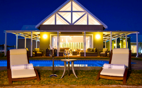 Eine Safari Lodge bei Nacht mit Pool im Vordergrund, Liegestühlen und beleuchtetem Gebäude im Hintergrund - Namibia Familienreise