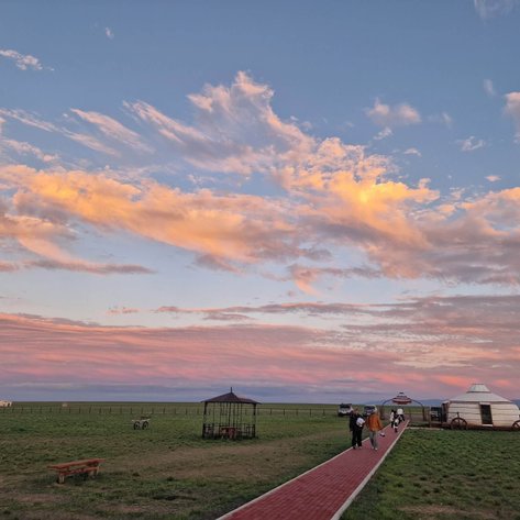 Eine malerische Landschaft mit sanften Hügeln, einem roten Weg und einem beeindruckenden Himmel voller pastellfarbener Wolken.