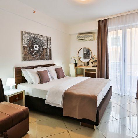 Ein modernes Hotelzimmer mit einem großen Bett, eleganten Kissen und einem gemütlichen Sessel in warmen Farbtönen.