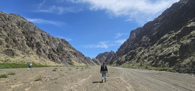 Eine Person wandert durch eine beeindruckende Schlucht, umgeben von steilen, felsigen Hängen und klarem, blauem Himmel.