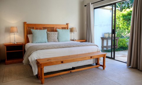 Ein helles Schlafzimmer mit einem großen Holzbett, dekoriert mit Kissen in sanften Farben und einem Blick auf den Garten.