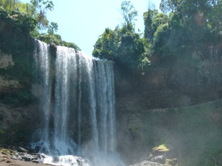 Ein majestätischer Wasserfall stürzt über eine Felswand, umgeben von üppigem Grün und sprühendem Wassernebel.