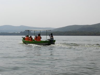 Eine Gruppe von Menschen in orangefarbenen Schwimmwesten fährt mit einem Boot über den ruhigen Naivasha-Kratersee.