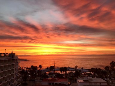 Ein atemberaubender Sonnenuntergang über dem Meer, mit leuchtenden orangefarbenen und roten Wolken am Himmel.