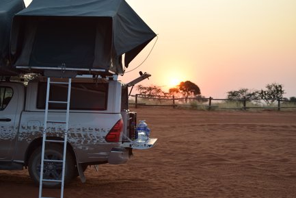 Ein Jeep steht mit aufgebautem Dachzelt auf Sand. Im Hintergrund der Sonnenuntergang - Namibia Familienreise