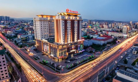Das Ramada Hotel in Ulaanbaatar erstrahlt in warmem Licht, umgeben von einer lebhaften Stadtlandschaft und fließendem Verkehr.