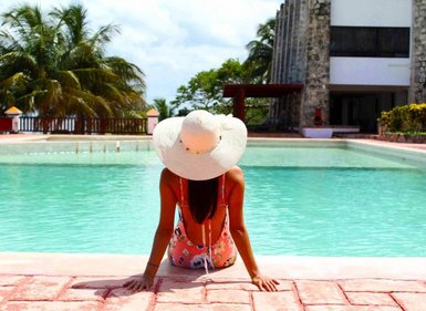 Eine Frau mit einem großen Sonnenhut sitzt am Rand eines Pools und genießt die entspannende Atmosphäre.