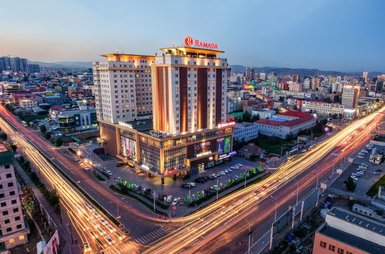 Das Ramada Hotel in Ulaanbaatar erstrahlt in warmem Licht, umgeben von einer lebhaften Stadtlandschaft und fließendem Verkehr.