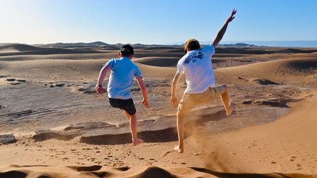 Kinder springen und haben Spaß auf den weiten Sanddünen der Sahara – Marokko Familienreise