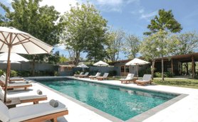 Ein einladender Poolbereich mit Liegen und Sonnenschirmen, umgeben von üppigem Grün und strahlend blauem Himmel.