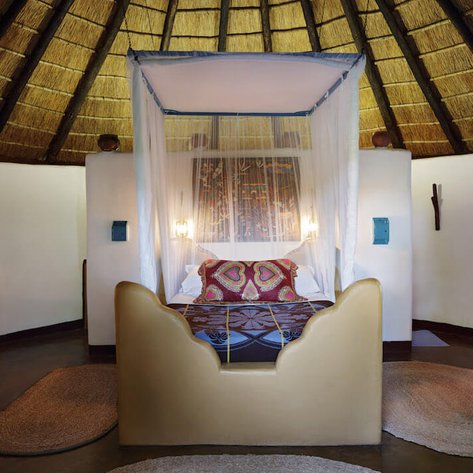 Ein gemütliches Zimmer mit Strohdach, zwei Betten und bunten Kissen, das eine entspannende Atmosphäre ausstrahlt.