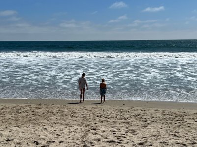 Zwei Kinder stehen am Strand von Santa Monica und beobachten die Wellen des Ozeans unter einem klaren blauen Himmel.