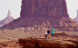 Drei Personen stehen auf einer Felsplattform in Monument Valley, umgeben von beeindruckenden roten Felsen und Hügeln.