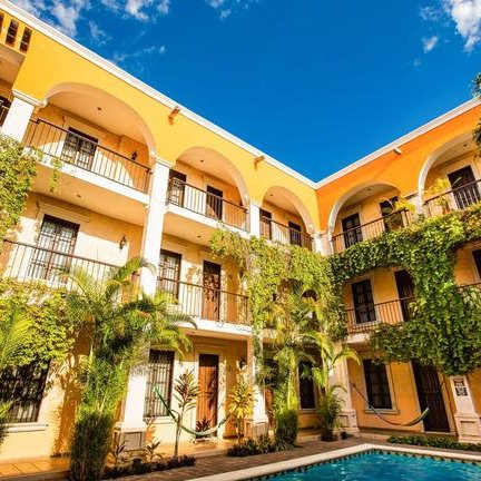 Ein sonniger Innenhof eines Hotels mit einem Pool, umgeben von üppigem Grün und bunten Gebäuden im kolonialen Stil.