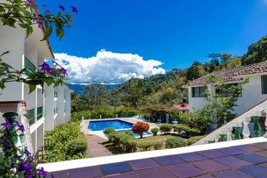 Ein malerischer Blick auf ein Hotel mit einem blauen Pool, umgeben von üppigem Grün und bunten Blumen im Vordergrund.