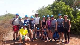 Eine Gruppe von Kletterern in Helmen posiert fröhlich im Freien, umgeben von grünen Sträuchern und sonnigem Himmel.