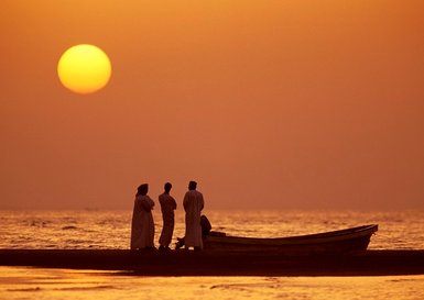 Omanis beobachten den Sonnenuntergang am Strand im Oman – Oman Reise mit Kindern