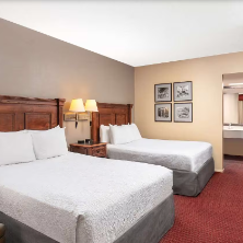 Ein gemütliches Hotelzimmer mit zwei Betten, warmen Holzmöbeln und einem einladenden Teppichboden.
