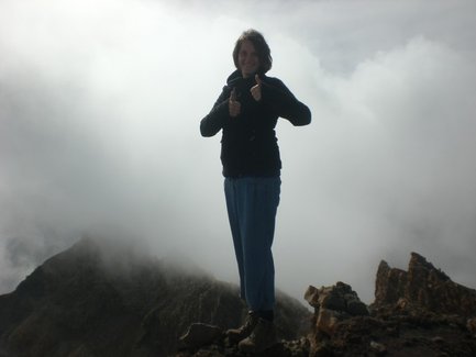 Eine Person steht auf einem Vulkan, umgeben von Wolken, und zeigt mit beiden Daumen nach oben, was Freude ausdrückt.