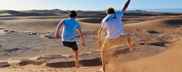 Kinder springen und haben Spaß auf den weiten Sanddünen der Sahara – Marokko Familienreise