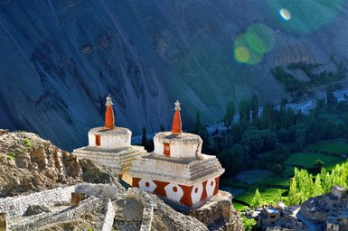 Zwei beeindruckende Stupas mit roten und weißen Mustern stehen majestätisch in einer bergigen Landschaft.