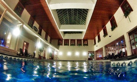Ein Innenpool mit klarem Wasser, umgeben von großen Fenstern und einer hohen Decke, die mit Holz verkleidet ist.