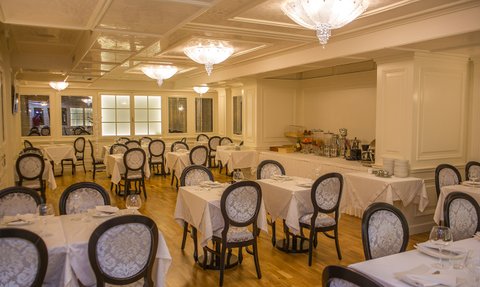 Elegante Restaurant mit weißen Tischen und stilvollen Stühlen, beleuchtet von funkelnden Kronleuchtern an der Decke.