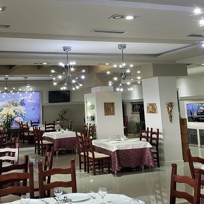Ein elegantes Restaurant mit weißen Tischdecken und Holzstühlen, beleuchtet von modernen Kronleuchtern.