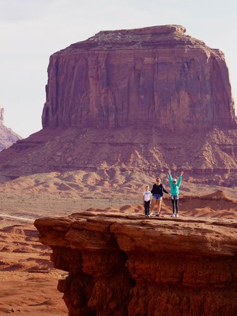 Drei Personen stehen auf einer Felsplattform in Monument Valley, umgeben von beeindruckenden roten Felsen und Hügeln.