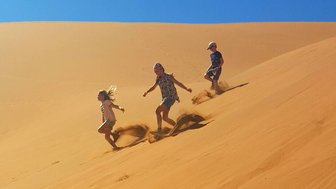 Drei Kinder laufen eine Düne hinunter - Namibia Rundreise mit Kindern