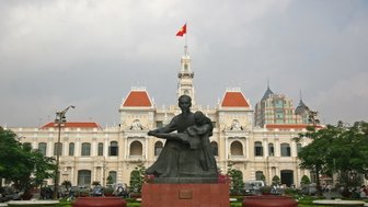 Eine Statue eines Mannes, der ein Kind hält, steht vor dem beeindruckenden Gebäude im Hintergrund mit der vietnamesischen Flagge.