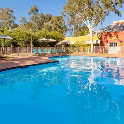 Ein klarer Swimmingpool umgeben von Liegen und Sonnenschirmen, einladend inmitten üppiger Bäume.