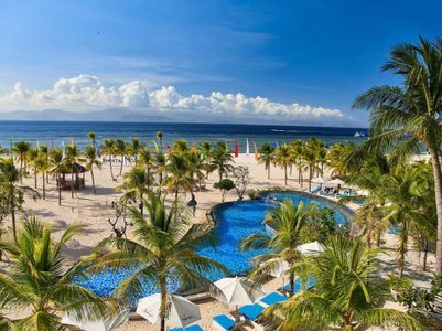 Ein atemberaubender Blick auf einen Pool, umgeben von Palmen und einem weißen Sandstrand unter einem strahlend blauen Himmel.