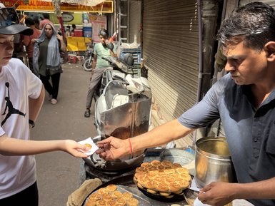 Ein Junge reicht einem Straßenverkäufer eine Bestellung, während köstliche Snacks auf einem Tisch in Delhi ausgestellt sind.
