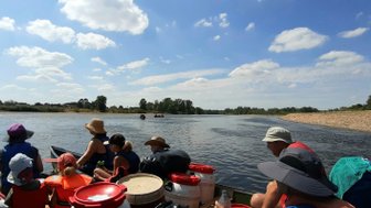 Eine Gruppe von Menschen sitzt in einem Kanu und genießt einen sonnigen Tag auf einem ruhigen Fluss mit blauen Himmel.