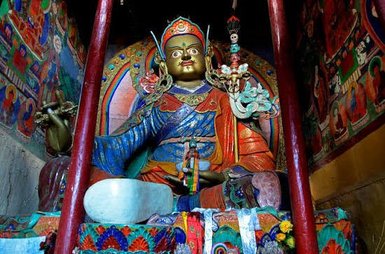 Eine majestätische Statue eines buddhistischen Gottes sitzt in einem kunstvoll dekorierten Raum mit bunten Wandmalereien.