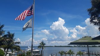 Eine amerikanische Flagge weht über einem malerischen Hafen mit Booten und üppigen Palmen im Vordergrund.