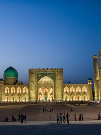 Die beeindruckende Architektur der Registan in Samarkand erstrahlt in warmem Licht, während Menschen die Szenerie genießen.