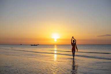 Eine Person steht am Strand und genießt den Sonnenuntergang, während sanfte Wellen den Sand umspülen.