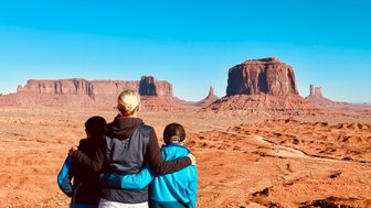 Drei Personen stehen mit dem Rücken zur Kamera und betrachten die beeindruckenden Felsformationen von Monument Valley.